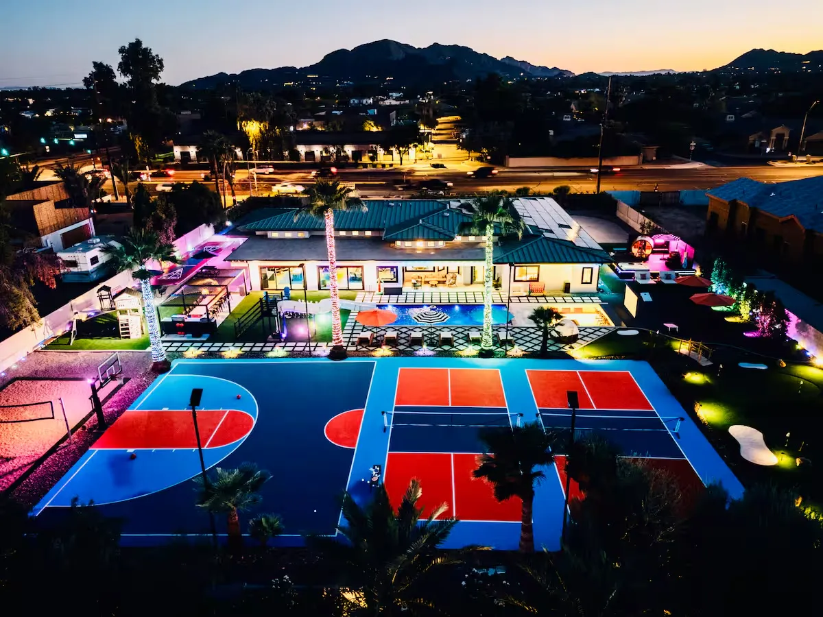 Desert home with a pool and basketball court lit up at night