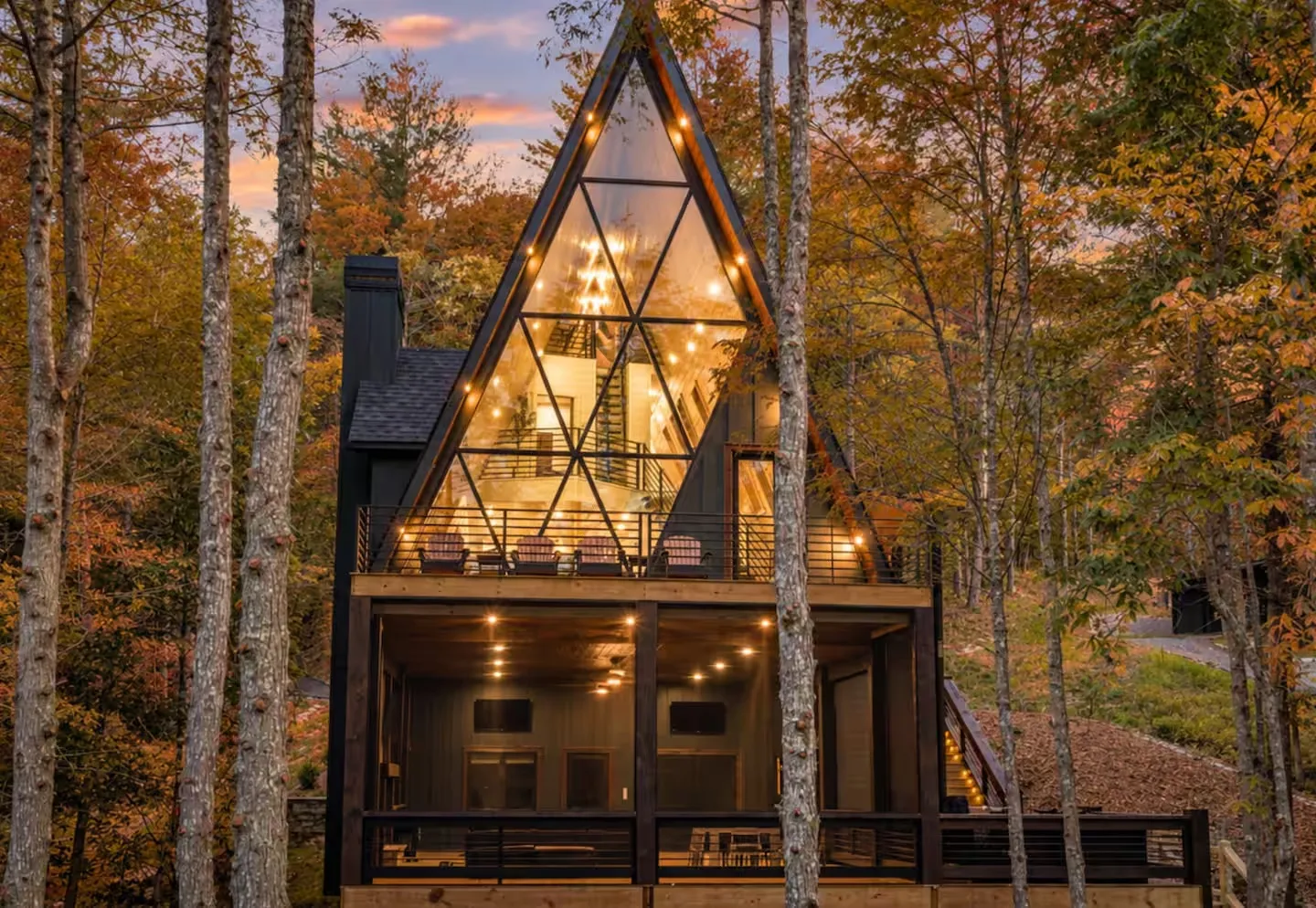 Glass-front A-frame cabin lit up among fall trees